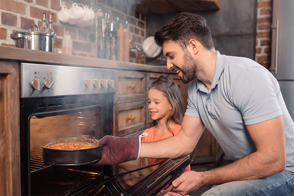 Pai e filha, tirando o bolo do forno e sorrindo